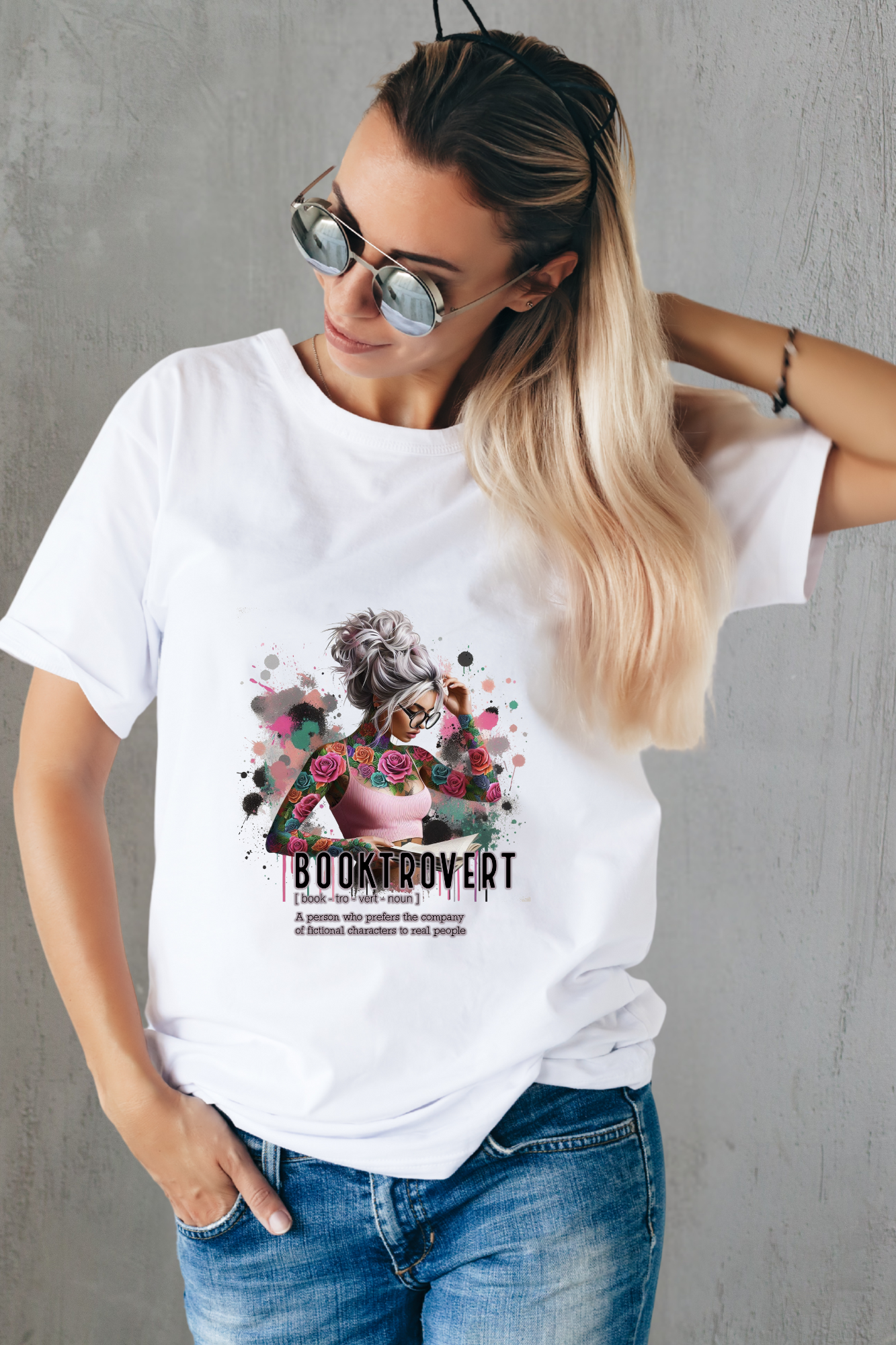 Woman wearing a white t-shirt with a graphic design and text, standing against a gray wall.