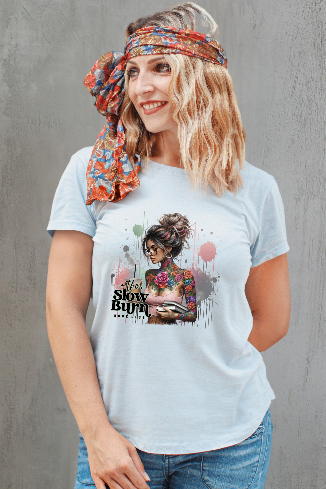 Woman wearing a light blue t-shirt with a graphic design and text, standing against a gray background.