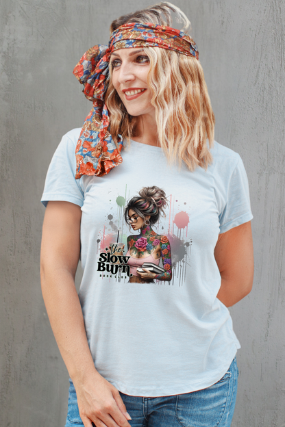 Woman wearing a light blue t-shirt with a graphic design and text, standing against a gray background.