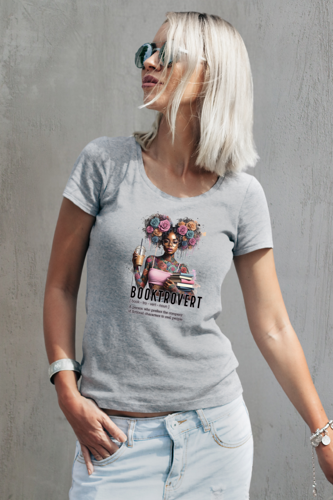 Woman wearing a gray t-shirt with a graphic design and text, standing against a gray wall.