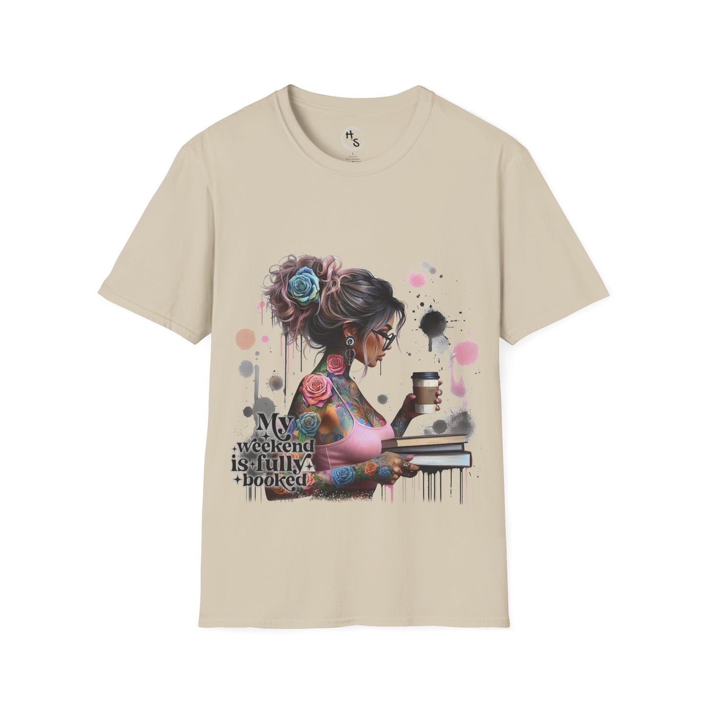 Beige t-shirt with a graphic design of a woman with tattoos and flowers, holding a coffee cup and book, on a beige background.