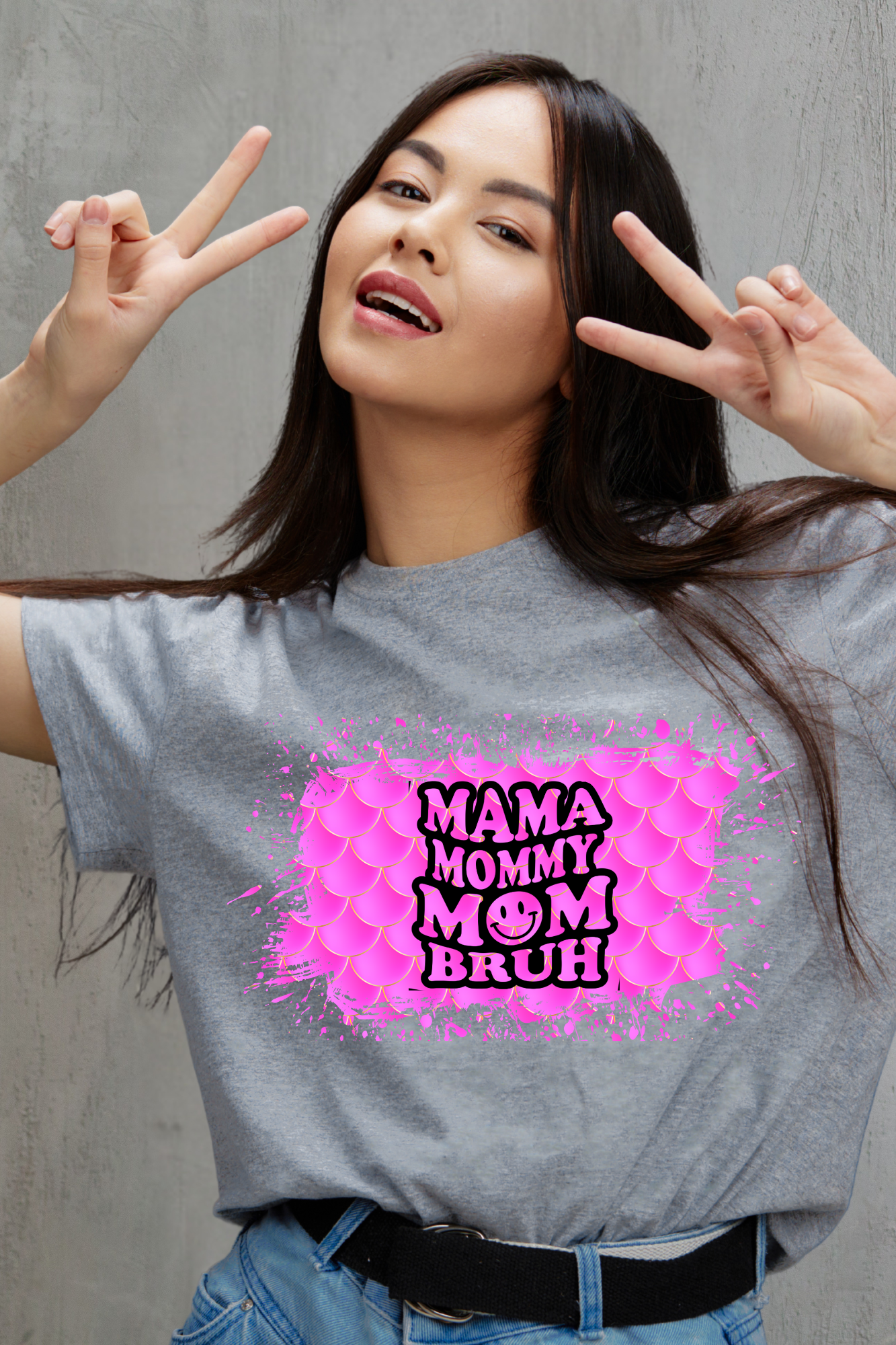 Woman wearing a gray t-shirt with pink and black text design, making peace signs.