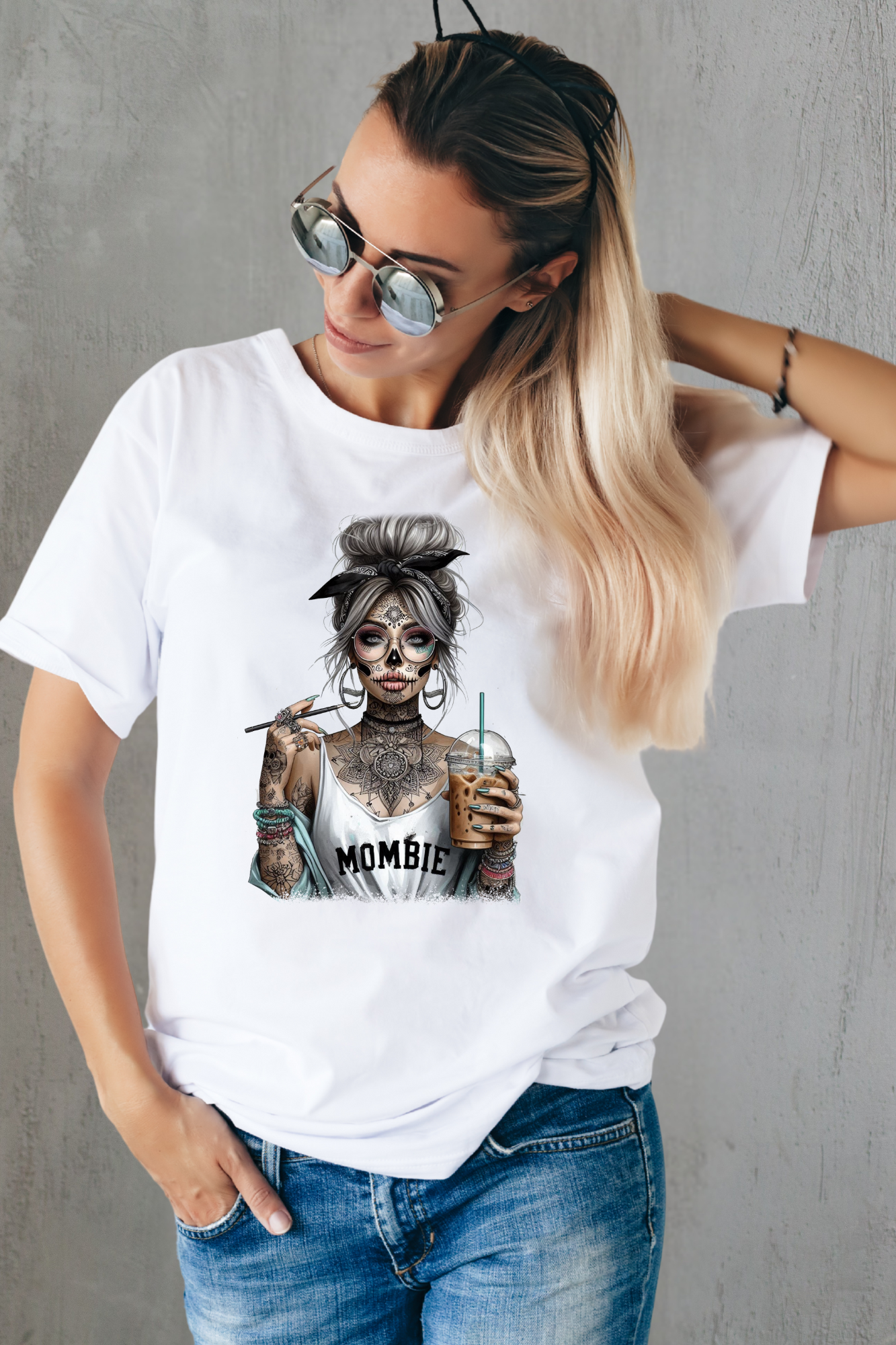 Woman wearing a white t-shirt with a graphic design of a zombie holding a drink, standing against a gray wall.