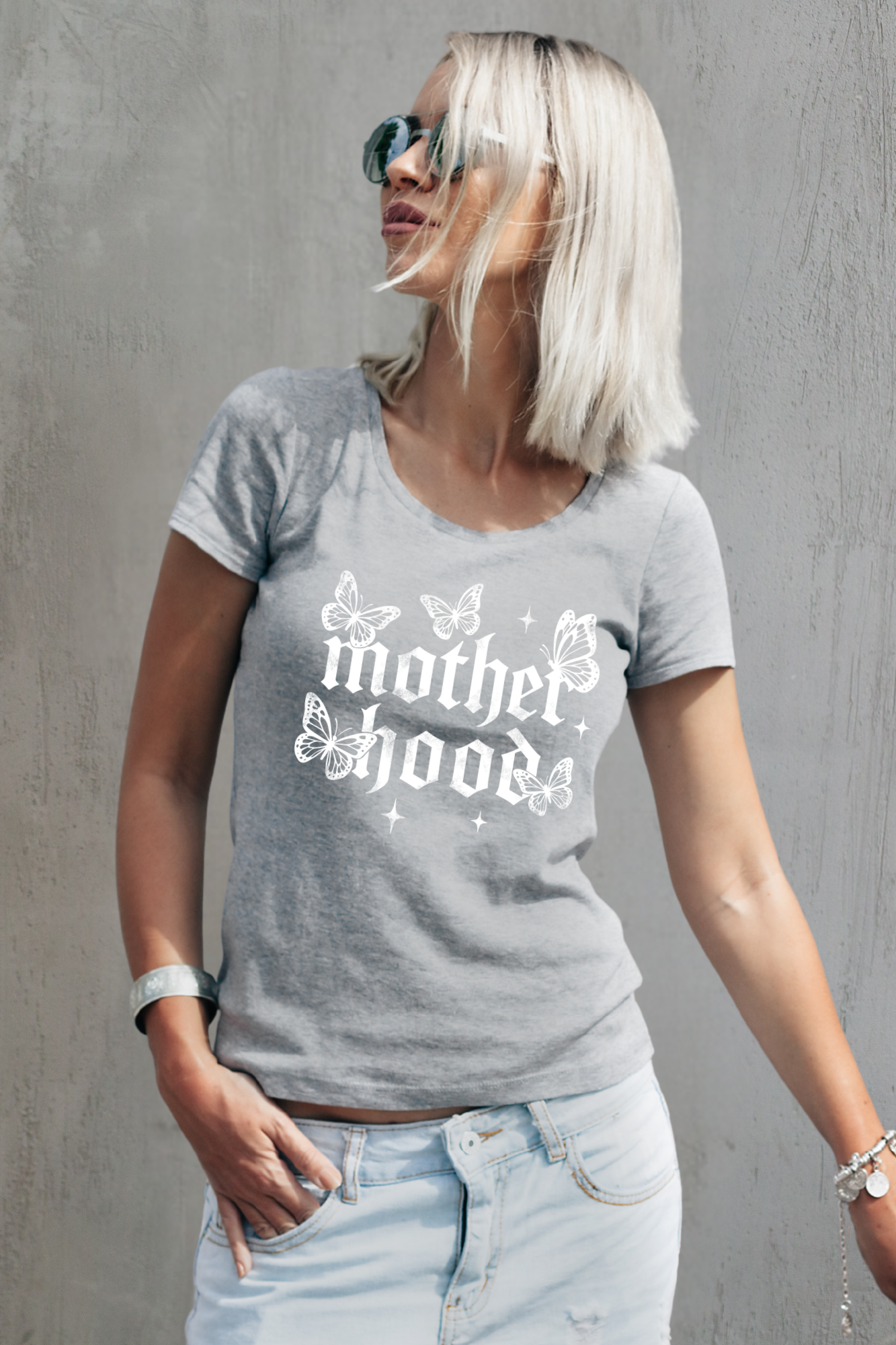 Grey gothic T-Shirt ‘Motherhood’ lettering surrounded by delicate white butterflies and small star accents on a light gray background