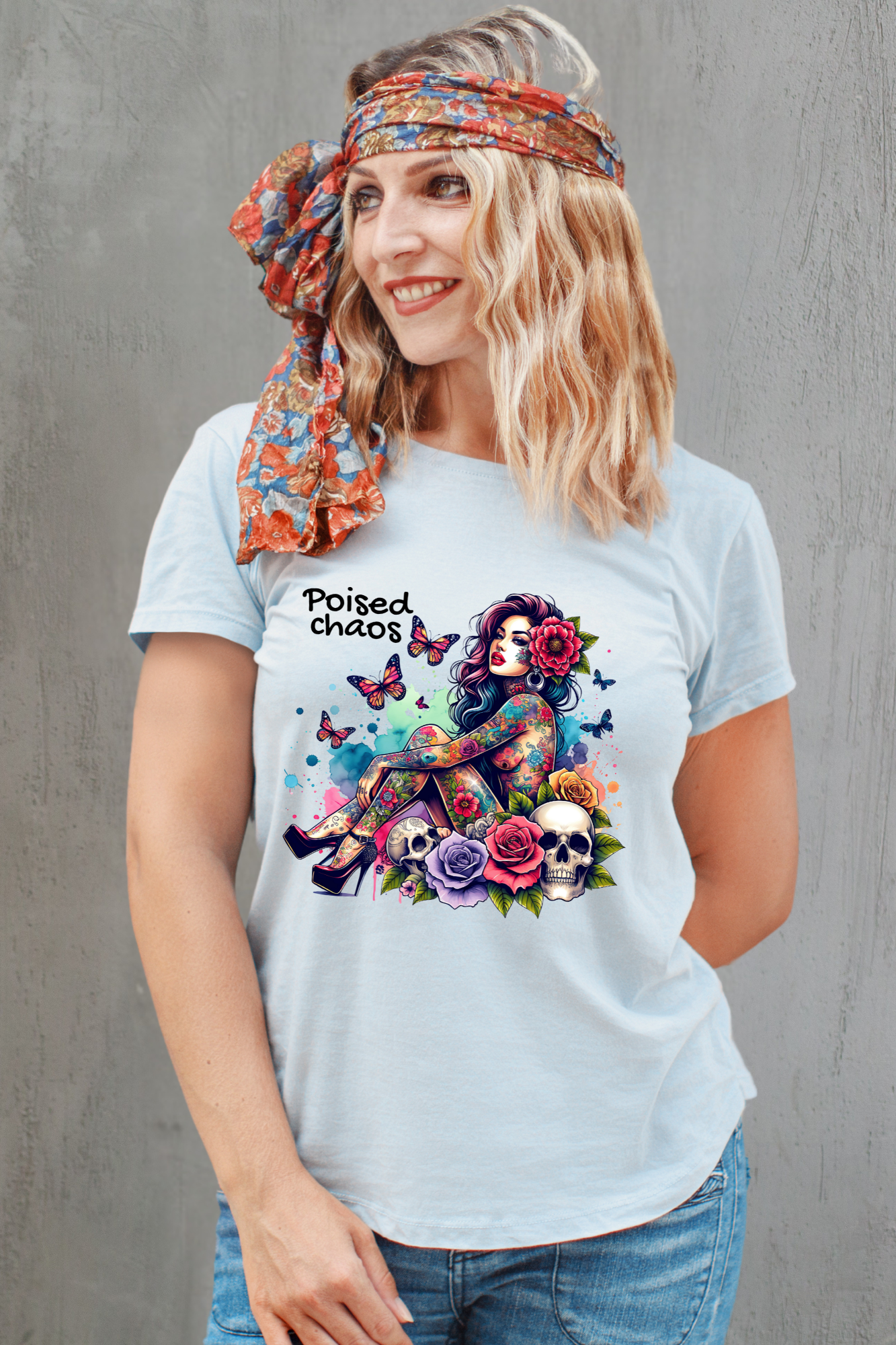 Woman wearing a grey t-shirt with colorful graphic design and text, standing against a gray concrete wall.