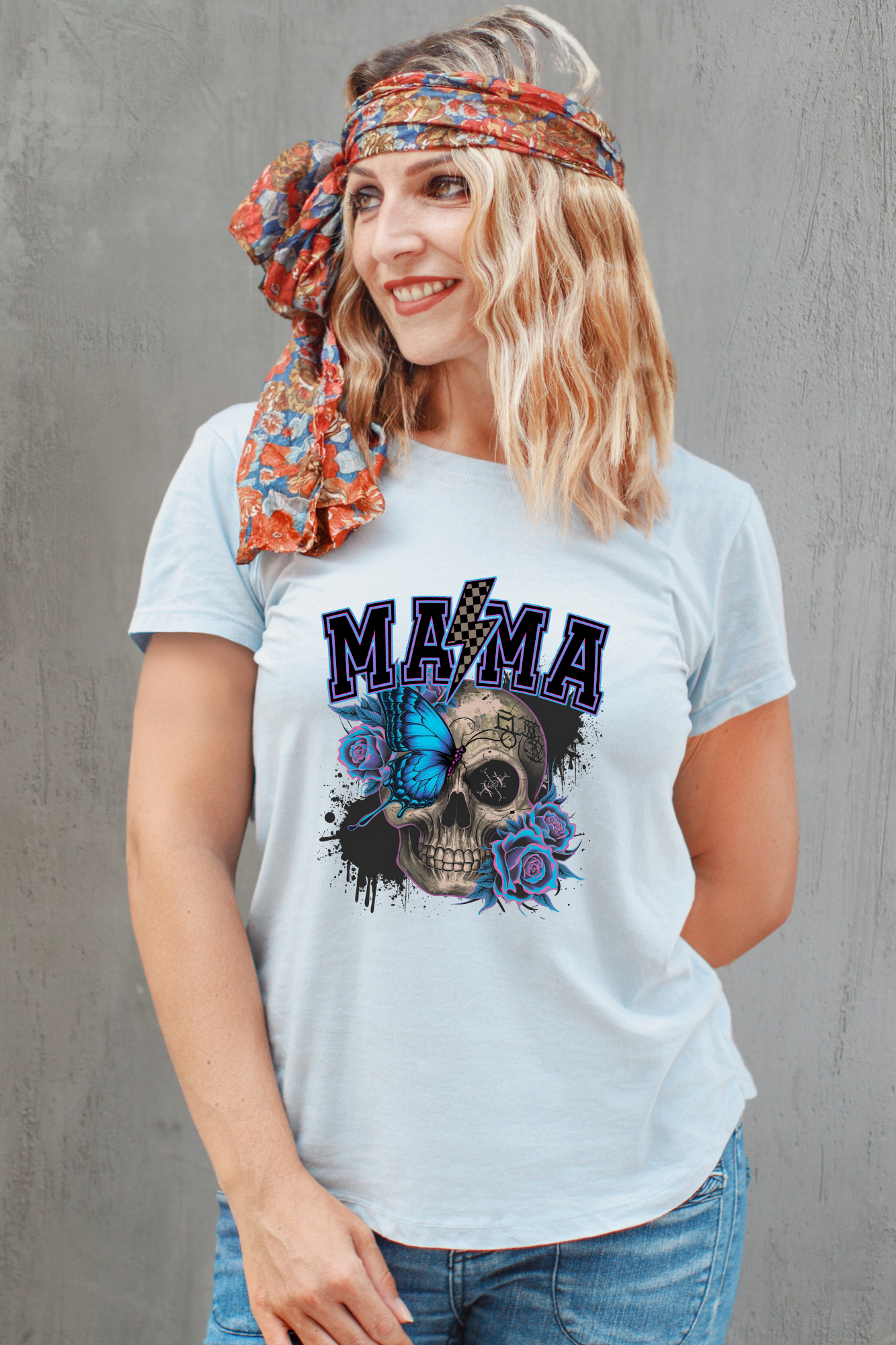 Woman wearing a light blue t-shirt with a skull design and 'MAMA' text, standing against a gray background.