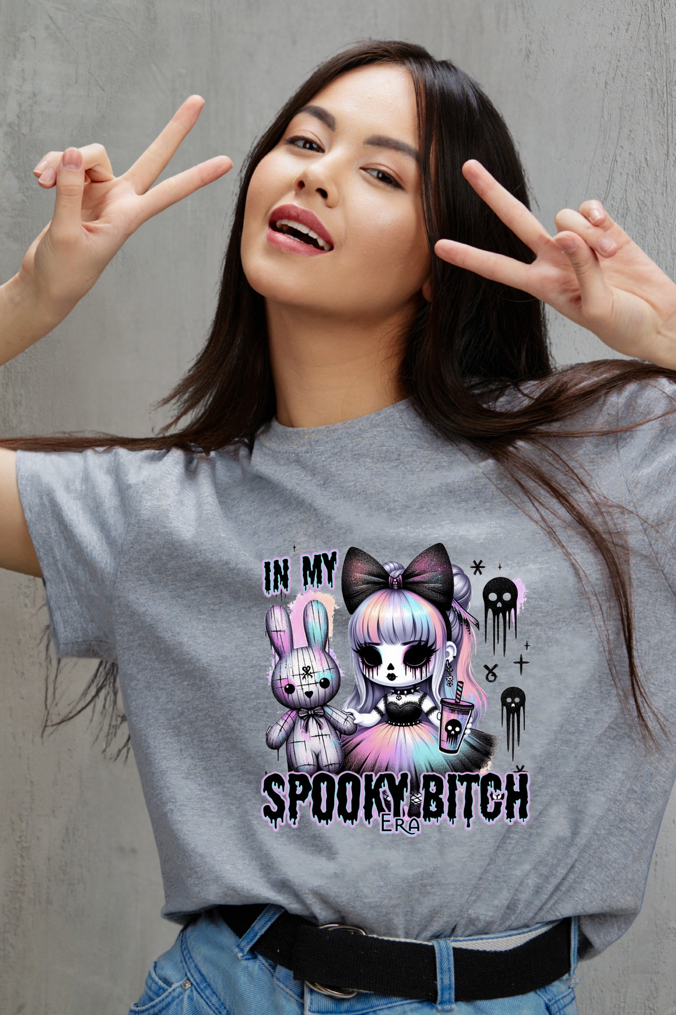 Woman wearing a gray t-shirt with a hallloween graphic design and text, making peace signs.
